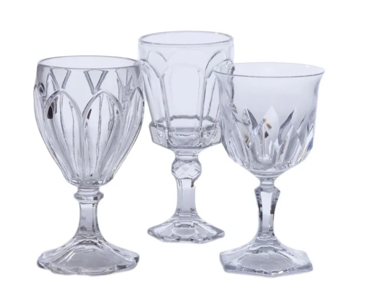 Three clear mismatched glass goblets in different vintage patterns and stem shapes on a white background