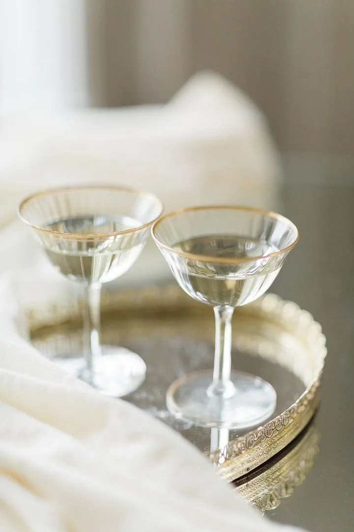 Ida Tray with Coupes WEBP Two vintage glass coupes with gold rims on a mirrored gold tray