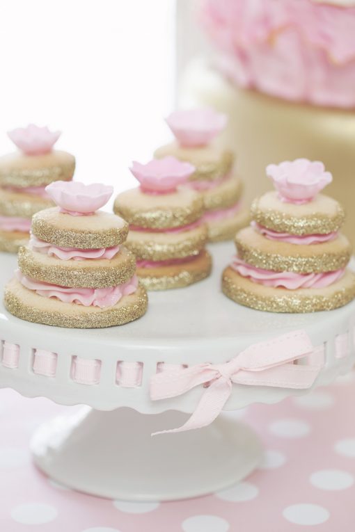 White porcelain pedestal cake stand with pink ribbon around the edge and sugar cookies on display