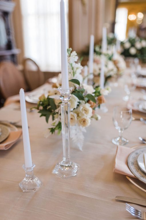 Glass candlesticks with white candles as part of an elegant tablescape with fine china