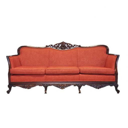 An orange-red vintage sofa with ornate dark wood edging and feet