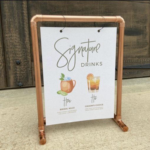 Copper pipes put together in a rectangle to hold a sign that says "signature drinks"