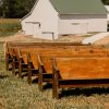 Wooden church pews set up outside on grass with a barn in the background