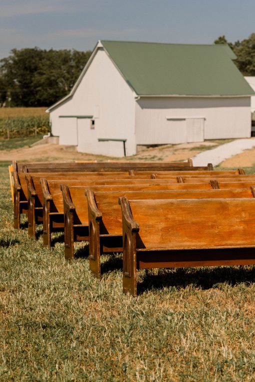 Wooden church pews set up outside on grass with a barn in the background