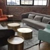 Lounge area at corporate event with two gray sofas, a sea-green wingback chair and gold round tables