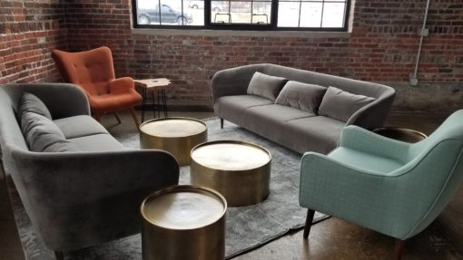 Lounge area at corporate event with two gray sofas, a sea-green wingback chair and gold round tables