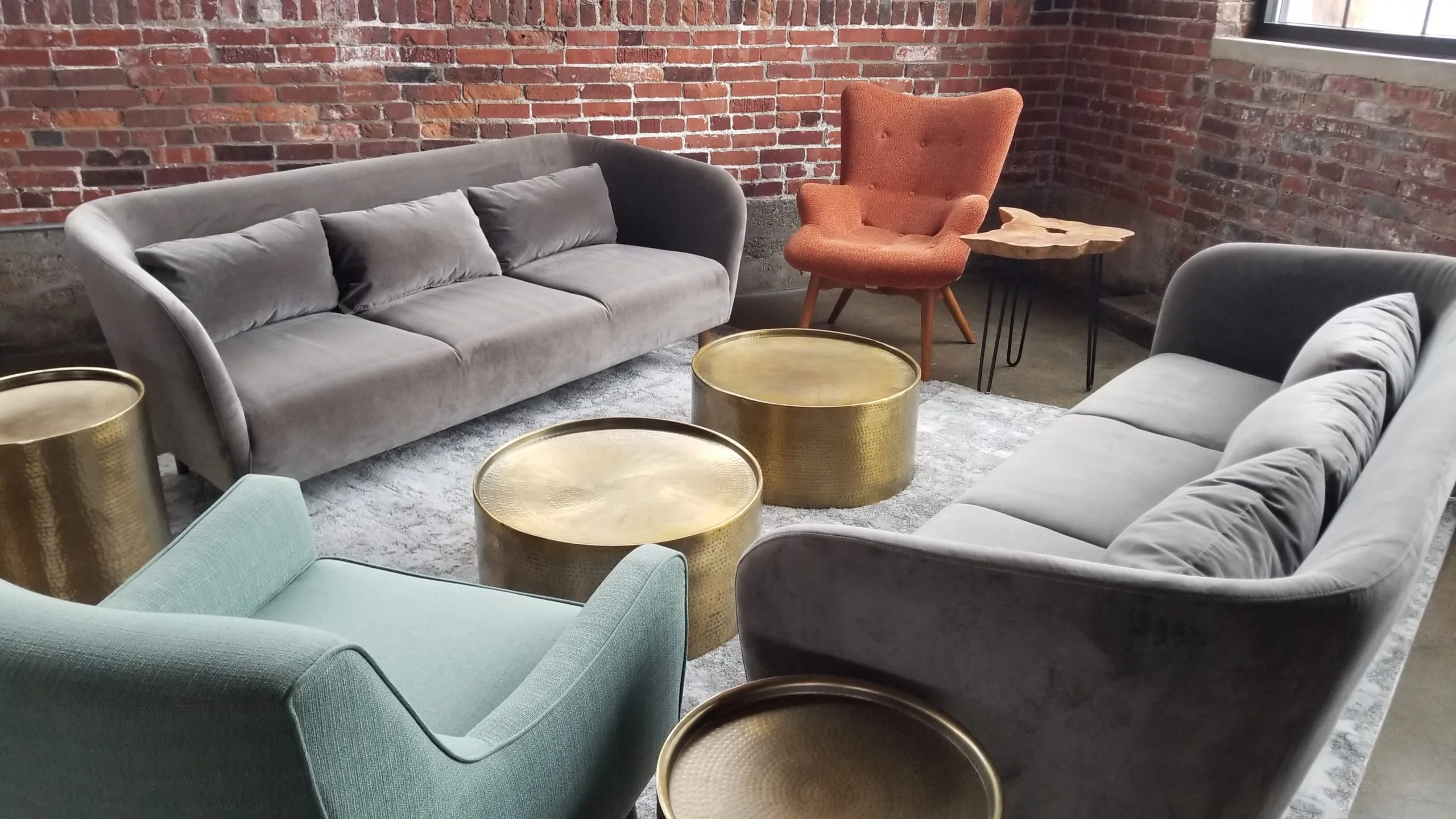 Lounge area for corporate event at Industry WEBP Lounge seating area at a corporate event with two modern gray sofas, an orange wingback arm chair, a seafoam green armchair and gold circular coffee tables