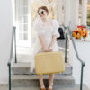 Woman in dress with sunglasses holding vintage suitcase on stairs