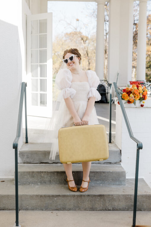 Woman in dress with sunglasses holding vintage suitcase on stairs