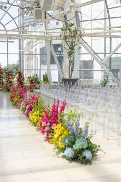 Clear ghost chairs arranged in a runway aisle with bright florals