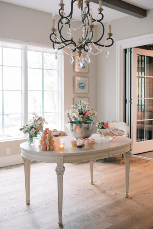 Cream colored oval vintage dining table with champagne bucket and florals. Bright window in the background.