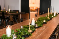 wooden farm table with greenery down the middle and votives and brass candlesticks