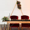 Sweetheart table with 2 deep red velvet high back armchairs behind. Sitting on a rug with tall candlesticks and florals