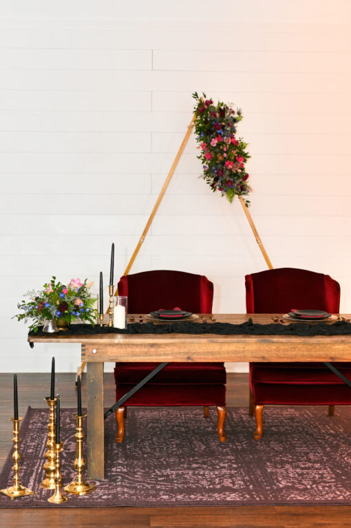 Sweetheart table with 2 deep red velvet high back armchairs behind. Sitting on a rug with tall candlesticks and florals