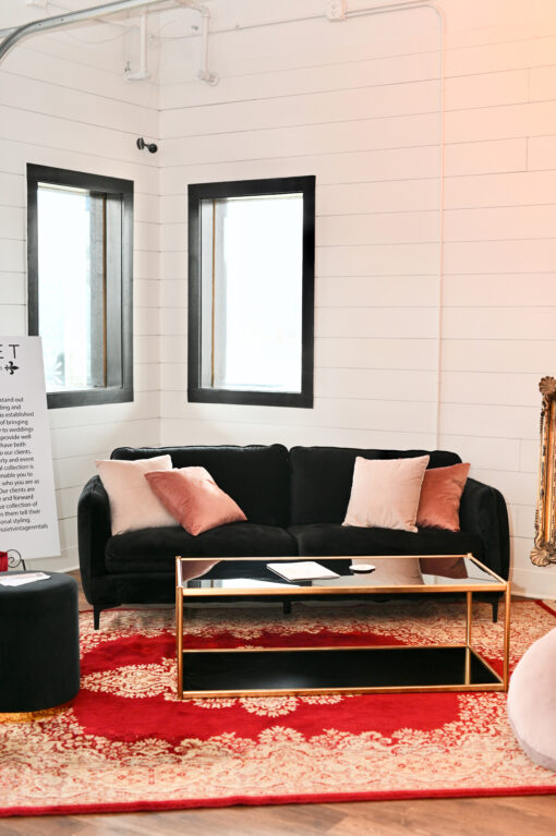 Black velvet sofa with soft pink pillows. Sitting on a red rug with a black glass coffee table.