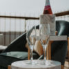 Round side table with marble top holding two champaign flutes. Behind it is a taller side table with a bottle.