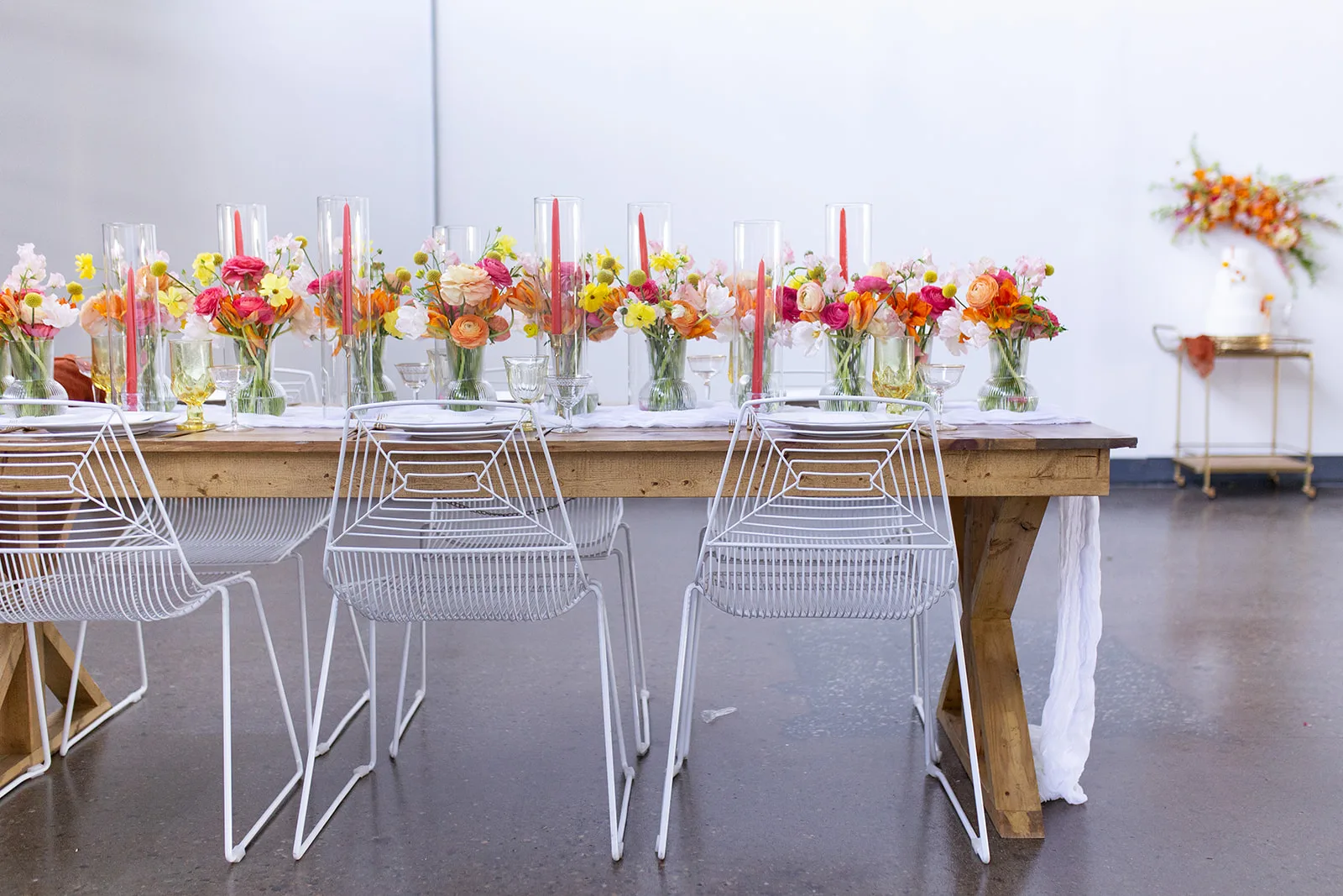 Tablescape with bright wedding florals WEBP Light color farm table with white wire chairs with bright