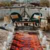 Long runner with red hues creating an aisle. Large glass cylinders with candles on the sides. Two chairs at the end with an industrial coffee table.