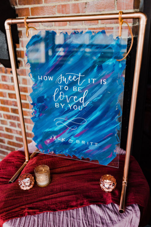 Table sign made out of copper pipes. Sign has a quote about love. On a table with votives at the bottom.