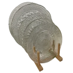 Variety of mismatched cut glass plates sitting upright in a wooden stand.