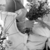 Black and white photo of a bride sitting on a vintage sofa. Wooden frame and velvet side highlighted. Bride holding florals.