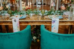 close up of headtable with wood farm table and two round velvet green chairs. florals and plates on the table