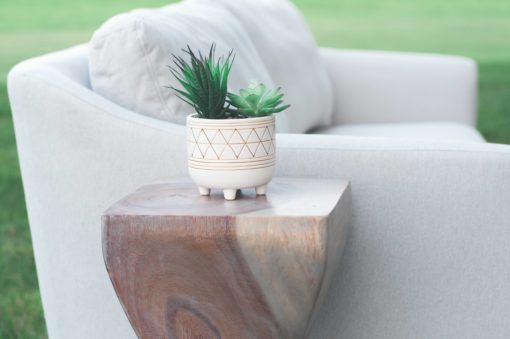 View of the side of a white modern sofa with a curved side table. Table has a square flat top and is holding a succulent plant in a white pot.