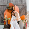 Couple posing for wedding photos in front of orange colored arched backdrop