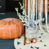 Leather pouf sitting next to copper stand, florals, and a large round jute rug.