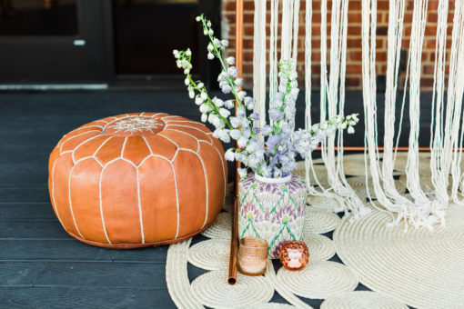 Leather pouf sitting next to copper stand, florals, and a large round jute rug.