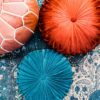 Arial close up of leather pouf, two round pillows - one teal and one rust - sitting on a teal rug.