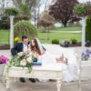 Couple sitting on white sofa with long rectangular coffee table in front. Columns in the back and florals on the table.