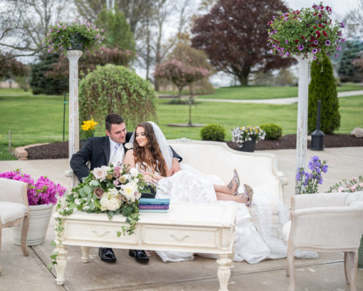 Couple sitting on white sofa with long rectangular coffee table in front. Columns in the back and florals on the table.