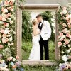 An 8 foot tall giant gold ornate frame with a bride and groom standing inside. Florals on the left and right. Outside on grass.