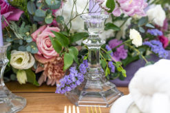Glass candlestick in a tablescape with purple and pink hued flowers in the background