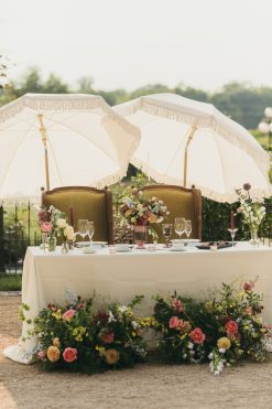 Wedding reception outdoors with headtable setup with decorated table, floral arrangements, and parasols. Two chartreuse accent chairs.
