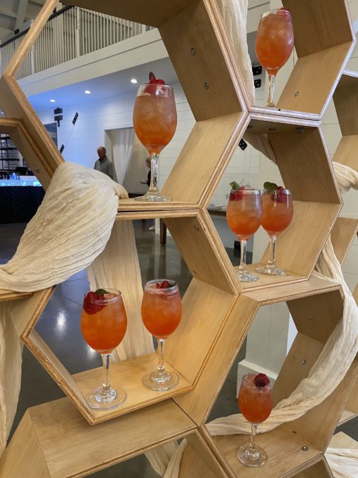 Close up of Honeycomb Wedding Backdrop Rental holding wineglasses with orange welcome drinks