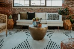 A modern lounge area with a plush cream sofa, a large patterned rug with black diamond shapes, and a gold coffee table. Part of an event rental display.