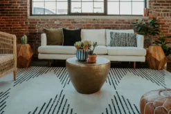 A modern lounge area with a plush cream sofa, a large patterned rug with black diamond shapes, and a gold coffee table. Part of an event rental display.