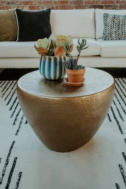 A close-up of a hammered gold coffee table decorated with a striped vase holding succulents and a small terracotta pot with lavender.