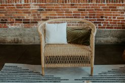 Rattan oversized chair with a square white pillow against a brick wall.