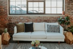 A modern lounge area with a plush cream sofa, a large patterned rug with black diamond shapes, and a gold coffee table. Part of an event rental display.