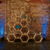 Honeycomb light wood backdrop with candles and flowers against a brick wall with blue lighting behind