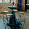 Four stools around a cocktail table draped in blue linen with florals on top