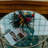 Top of a round glass coffee table with florals. Looks through onto a rug with teal and off white coloring