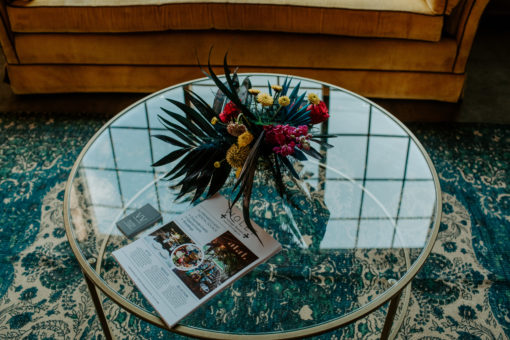 Top of a round glass coffee table with florals. Looks through onto a rug with teal and off white coloring