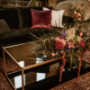 Black glass coffee table with gold edging on a rug. Autumn colored flowers on the table.