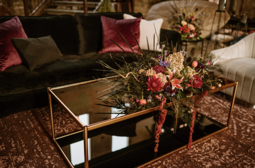 Black glass coffee table with gold edging on a rug. Autumn colored flowers on the table.