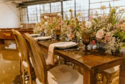 Solid wood farm table, french wooden chairs with cushions - set up for a wedding reception with florals and place settings