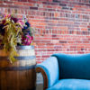 Vintage wine barrel used as a side table next to an antique blue velvet couch. Florals on the barrel. Styled lounge setting at a launch party.